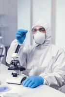 Microbiologist dressed in ppe suit analyzing sample on microscope glass slide Examining vaccine evolution using high tech for researching treatment against covid19 virus. photo