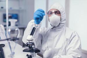 Scientist looking at a microscope slide dressed in coverall during coronavirus. Examining vaccine evolution using high tech for researching treatment against covid19 virus. photo