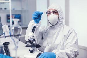 Experienced medical researche analyizing blodd sample on microscop glass slide dressed in ppe. Examining vaccine evolution using high tech for researching treatment against covid19 virus. photo