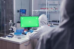 Over shoulder shot of researcher typing on computer with copy space available during coronavirus in laboratory. Team of microbiologists doing vaccine research writing on device with chroma key, isolated, mockup display. photo