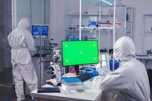 Medic researcher typing on computer keyboard with green screen Team of microbiologists doing vaccine research writing on device with chroma key, isolated, mockup display. photo