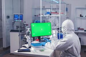 Engineer in laborator during coronavirus pandemic working on computer with green screen. Team of microbiologists doing vaccine research writing on device with chroma key, isolated, mockup display. photo