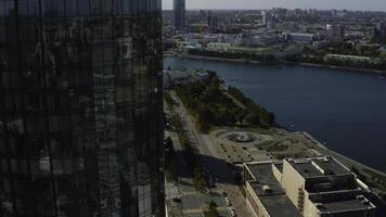 Top view of glass facade of high-rise building with landscape of city and river. Stock footage. Beautiful landscape of modern city with glass buildings. Glass skyscrapers with green landscapes of photo