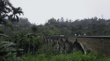 personas caminar en puente en selva montañas. acción. hermosa paisaje con Roca puente en Valle de montaña selva. puente en selva con turistas caminando en nublado día foto