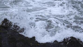 de cerca de oleada de olas en rocoso costa. acortar. hermosa olas con chapoteo rodar en piedras de costa. hermosa salpicaduras de olas estrellarse en rocas en nublado día foto