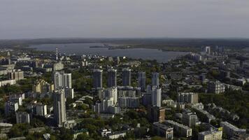 City with high-rise buildings on background of lake and green forest. Stock footage. Modern buildings in beautiful green city with lake and forest horizon. Top view of panorama of modern city in photo