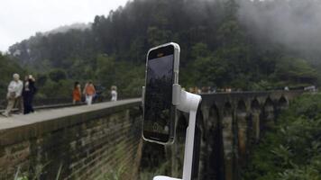 Shooting on tripod phone while traveling. Action. Shooting video on phone with stabilizer while traveling. Shooting bridge with railway in jungle on phone for blog photo