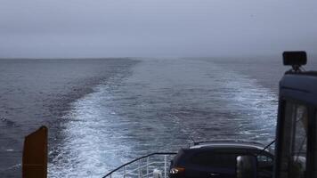 Ship with car sails into sea in cloudy weather. Clip. Sailing on ferry with car in sea. View of line left by sailing ship at sea on cloudy day photo