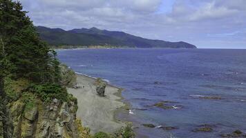 Beautiful view of bend of coast with rocks on sunny day. Clip. Landscape of rocky coast with green mountains and forest. Beautiful beach with rocks and blue sea on sunny day photo