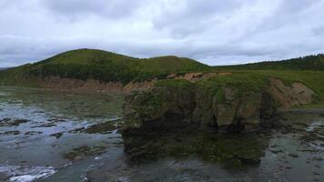 Top view of rocky coast with algae on shore. Clip. Landscape of rocks on coast with algae on background of mountains in cloudy weather. Diversity of flora of sea coast with rocky mountains photo