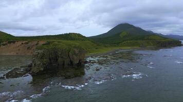 Top view of rocky coast with algae on shore. Clip. Landscape of rocks on coast with algae on background of mountains in cloudy weather. Diversity of flora of sea coast with rocky mountains photo