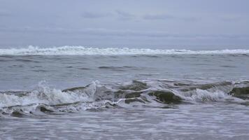 Seascape of beautiful waves on cloudy day. Clip. Beautiful coastal waves on background of horizon with cloudy sky. Coastal waves of North Sea on cloudy day photo