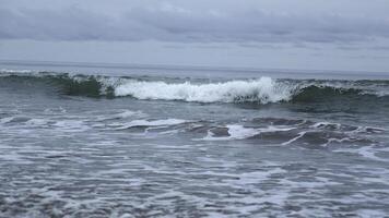 Seascape of beautiful waves on cloudy day. Clip. Beautiful coastal waves on background of horizon with cloudy sky. Coastal waves of North Sea on cloudy day photo