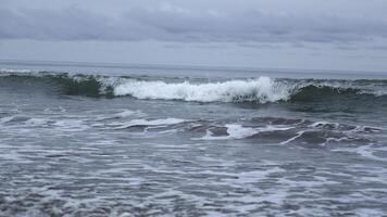 Seascape of beautiful waves on cloudy day. Clip. Beautiful coastal waves on background of horizon with cloudy sky. Coastal waves of North Sea on cloudy day photo