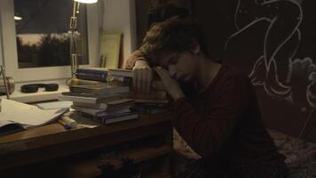 Tired student falls asleep on stack of books. Stock footage. Tired young man prepares for exam and falls asleep. Student prepares for exam and falls asleep on books at night photo