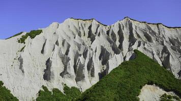 Amazing white mountains with green grass. Clip. Beautiful patterns on rocky white mountain with bright greenery on sunny summer day. White rocks of volcanic origin on island on summer day photo