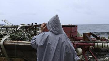 Man walks along pier to fishing boat. Clip. Man on stone pier goes to fishing boat. Man walks along embankment with fishing boats on cloudy day photo