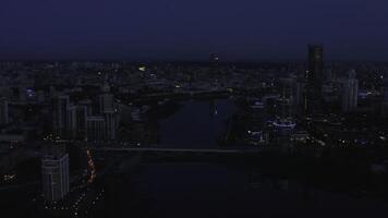 Top view of landscape of evening city with lanterns and river. Stock footage. Beautiful panorama of city with reflection of sunset light on glass skyscrapers. Dark twilight over glowing metropolis photo