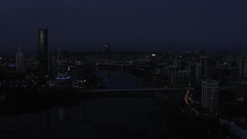 Top view of landscape of evening city with lanterns and river. Stock footage. Beautiful panorama of city with reflection of sunset light on glass skyscrapers. Dark twilight over glowing metropolis photo