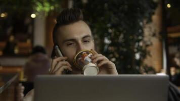 joven hombre es trabajando en ordenador portátil en café y hablando en teléfono. valores imágenes. joven persona de libre dedicación es trabajando en ordenador portátil y respondiendo llamadas remoto trabajo con ordenador portátil y café llamadas foto