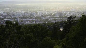 Beautiful view of cable car with view of town in summer. Clip. Green forest on slope with moving cable ways on edge of town. Beautiful city in valley with cable car on sunny summer day photo