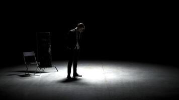 Man in suit alone on theater stage. Stock footage. Single attractive man in suit is playing on stage of theater. Man in suit with mirror is alone on dark theatrical stage photo