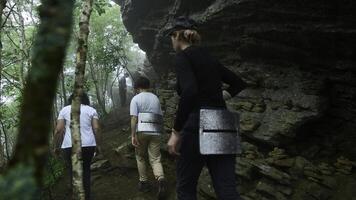 Group of tourists is walking along mountain trail in forest. Clip. Active tourists walk along trail in dense forest with rocks. Tourists go on difficult hiking route in forest with rocks photo