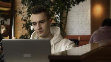joven hombre es concentrando en ordenador portátil en cafetería. valores imágenes. estudiante es escritura papel en ordenador portátil en cafetería. hermoso joven hombre independiente a ordenador portátil en café foto