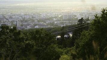 Beautiful view of cable car with view of town in summer. Clip. Green forest on slope with moving cable ways on edge of town. Beautiful city in valley with cable car on sunny summer day photo