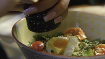 Close-up of woman adding spices to salad. Stock footage. Woman pepper salad with egg. Hearty seasoned salad or bowl with beautiful serving photo
