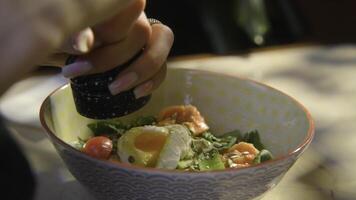 Close-up of woman adding spices to salad. Stock footage. Woman pepper salad with egg. Hearty seasoned salad or bowl with beautiful serving photo