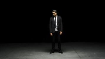 Man in suit stands emotionally on stage. Stock footage. Man in suit stands on stage with dramatic look. Elegant dramatic man on dark stage in emotional production photo