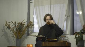 Young man is reading book and drinking tea in cafe. Media. Handsome young man is drinking tea and reading book alone. Guy is reading book in cozy cafe photo