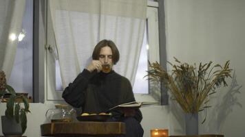 joven hombre es leyendo libro y Bebiendo té en cafetería. medios de comunicación. hermoso joven hombre es Bebiendo té y leyendo libro solo. chico es leyendo libro en acogedor café foto