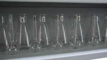 multiple laboratory flasks on the shelf ready to be used. Clip. Hand of a doctor or scientist in glove taking one empty glass flask. photo