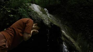 joven mujer Bebiendo agua desde cascada cascada a profundo tropical lluvia bosque. creativo. hembra caminante Bebiendo agua desde montañoso primavera. foto