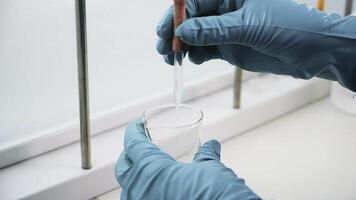 Close up of transparent liquid being poured into a bottle with a pipette on a white background. Clip. Hands in gloves pressing on a pipette. photo