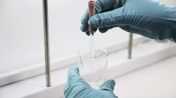 Close up of transparent liquid being poured into a bottle with a pipette on a white background. Clip. Hands in gloves pressing on a pipette. photo