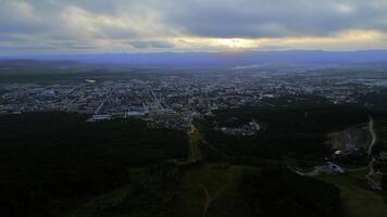 Aerial of the city and big green hills. Clip. Summer big city and cloudy sky during sunset. photo