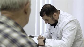 mayor masculino paciente hablando con hombre médico en el oficina. acortar. escritura prescripción a mayor paciente. foto