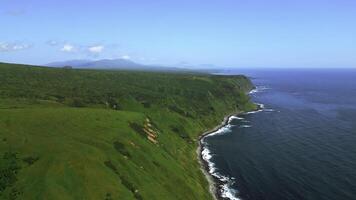 Wild nature, green mountains with steep green slopes leading to the sea. Clip. Aerial of foam of blue waves break in volcanic rocks. photo