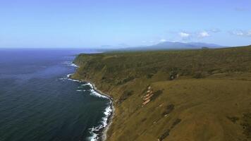 Autumn sunny day on the shore with smooth sea waves. Clip. Aerial view of hills covered by withered grass and dark blue sea. photo