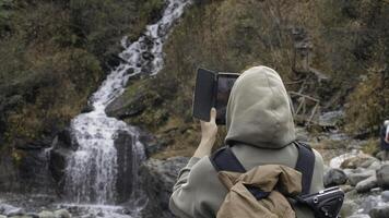 cascada fluye terminado el rocas a el río. creativo. caminante tomando foto de frío montañoso corriente en teléfono inteligente en otoño bosque.