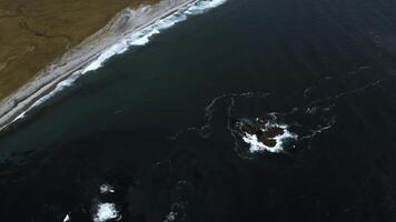 Aerial top view of waves break on rocks in a blue ocean. Clip. Ocean waves crashing against an empty stone rock cliff. photo