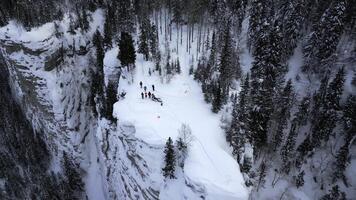 Winter mountain cliff covered by snow, ice, and fur trees. Clip. Stunning frozen winter nature, aerial view of tourists enjoying the day on the cliff edge. photo
