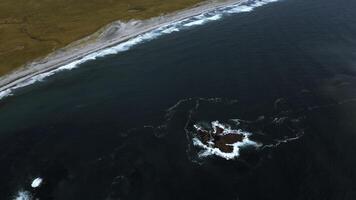 Aerial top view of waves break on rocks in a blue ocean. Clip. Ocean waves crashing against an empty stone rock cliff. photo