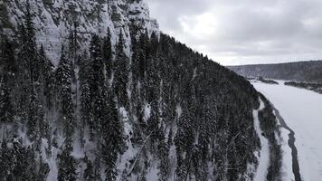 Winter mountain cliff covered by snow, ice, and fur trees. Clip. Stunning frozen winter nature, aerial view. photo