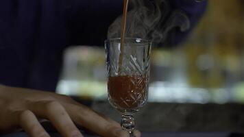 Close up of bartender at a bar counter pouring alcohol into vintage glass. Media. Pouring red hot alcoholic tincture with steam. photo