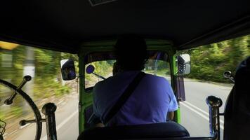 Rear view of a tuk-tuk or motorcycle driver carrying passengers along green trees and cars. Action. Concept of travelling. photo