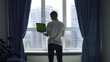 Back view of a young man in white t shirt working on laptop with green chroma key screen. Media. Concept of using modern technologies for remote work. photo